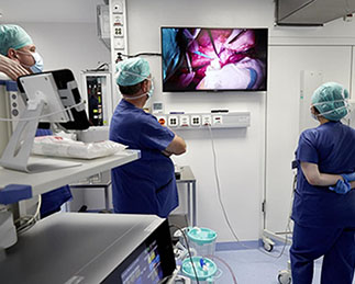 Personen mit Schutzmasken beobachten einen medizinischen Einsatz am Bildschirm